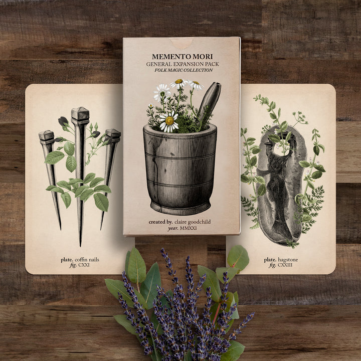The Folk Magic expansion pack and two cards (coffin nails and hagstone) against a wooden background with lavender flowers below
