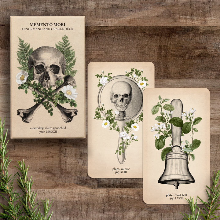 The box and two cards (mirror and mort bell) against a wooden background with rosemary sprigs