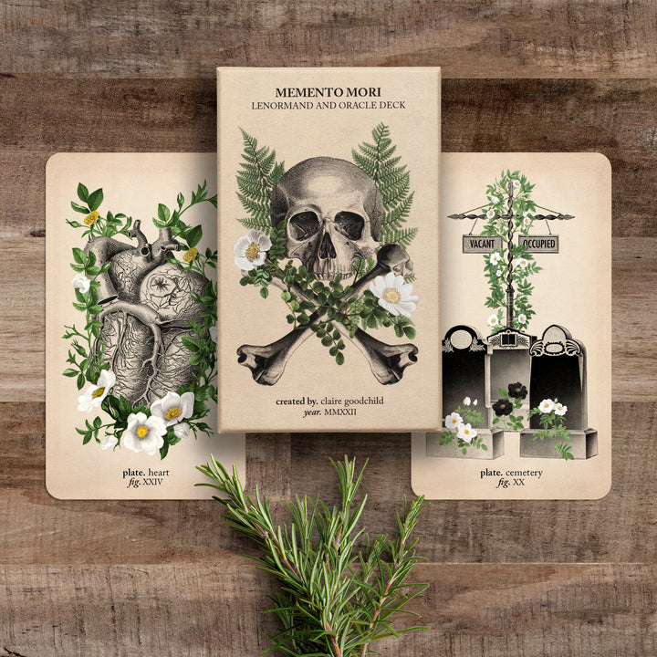 The oracle deck and two cards (hearty and cemetery) against a wooden background with rosemary sprigs below them